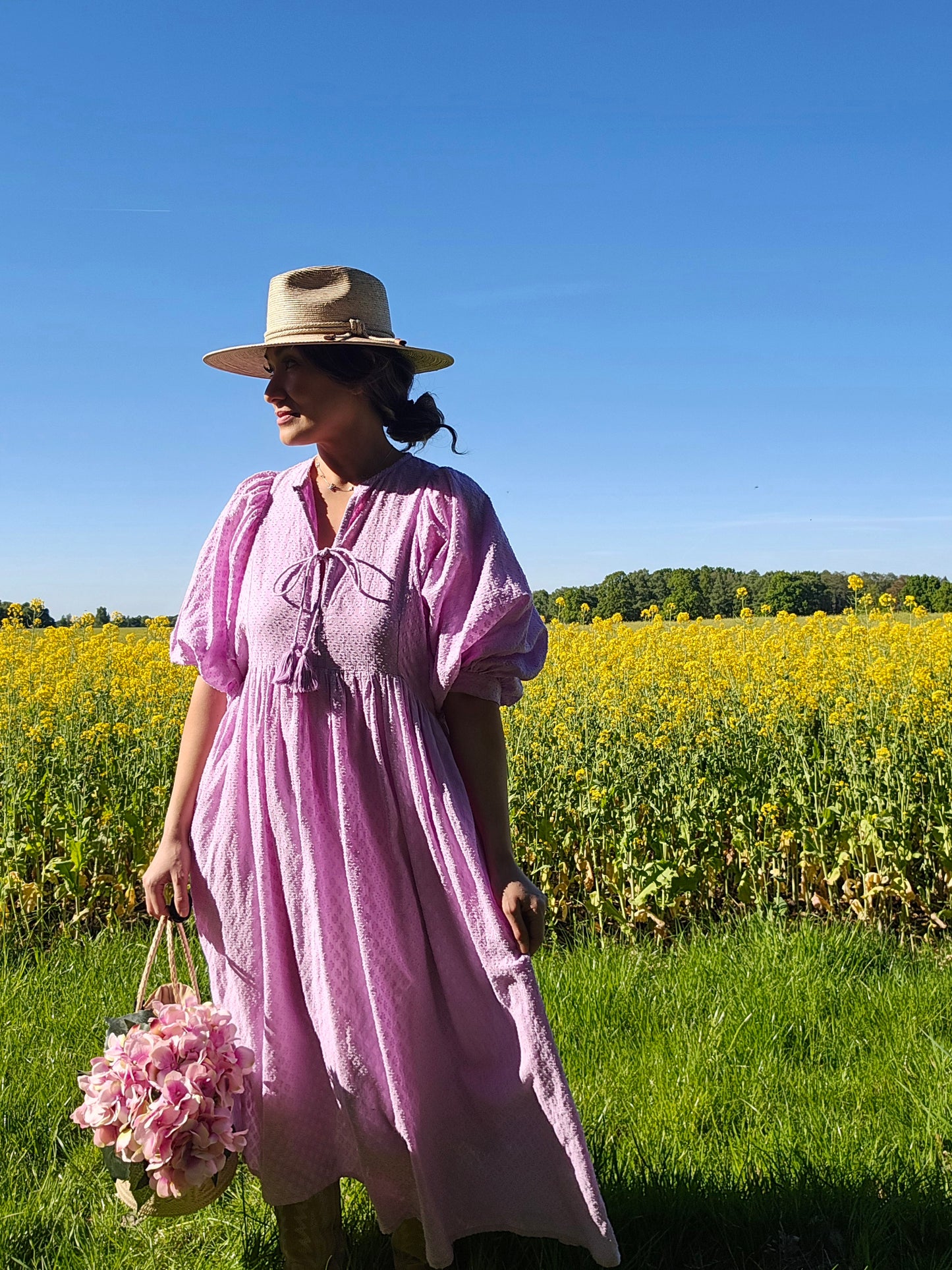 Modell trägt das lila Lucia Midikleid in einem Blumenfeld, ideal für Sommerausflüge und Freizeit.
