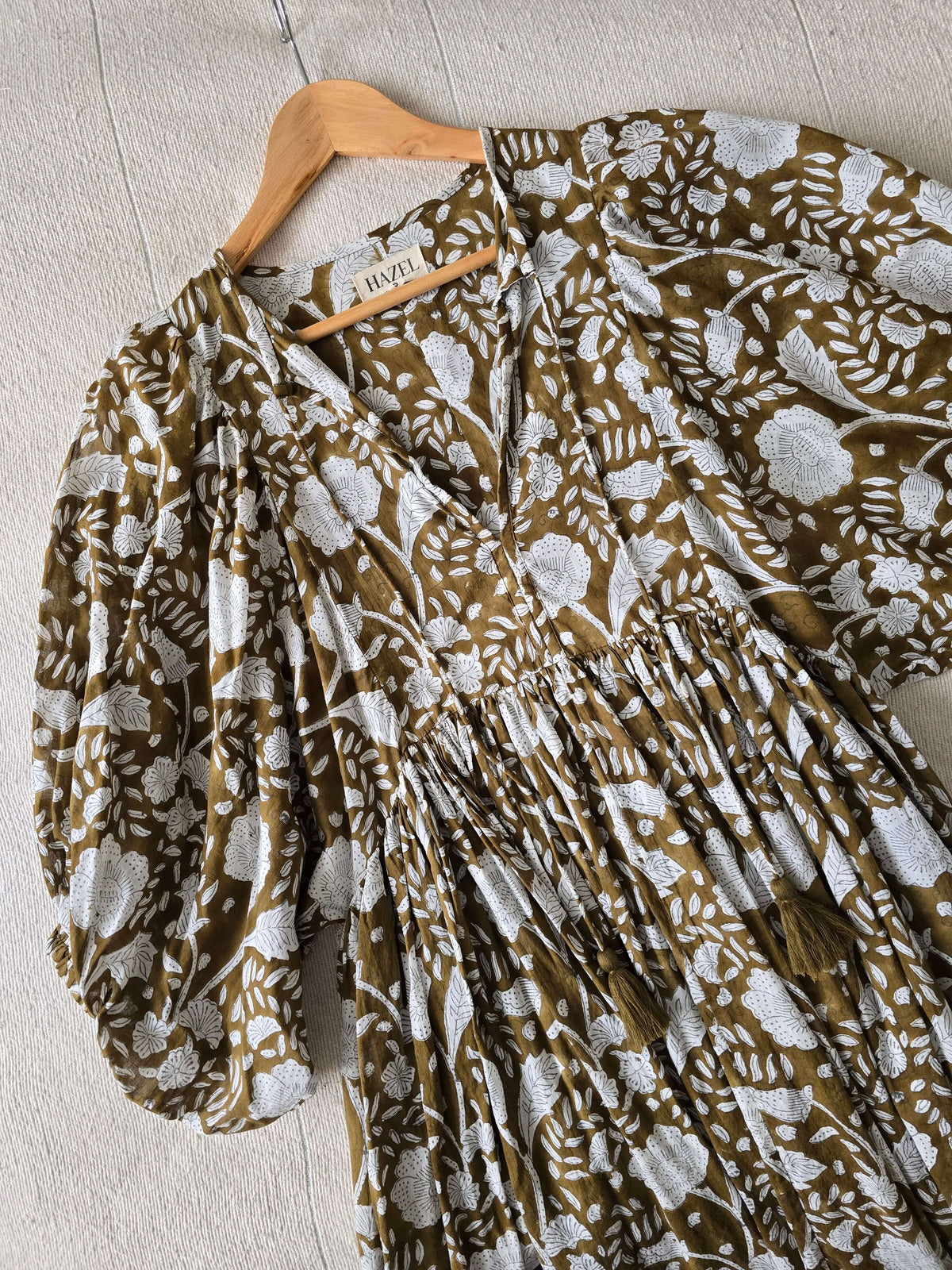Camilla Kleid Braun mit Handblockdruck – Fließendes, Blumiges Midi-Baumwollkleid auf einem Holzkleiderbügel.