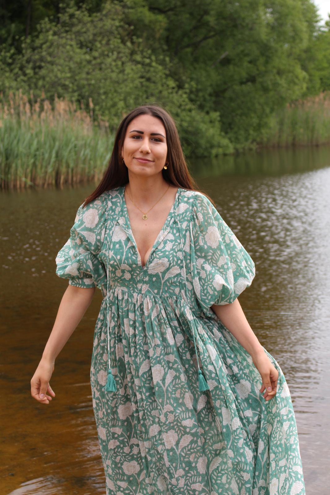 Frau trägt das Camilla Kleid in Misty Jade, Vintage-inspiriert mit floralem Handdruck, am Wasser.