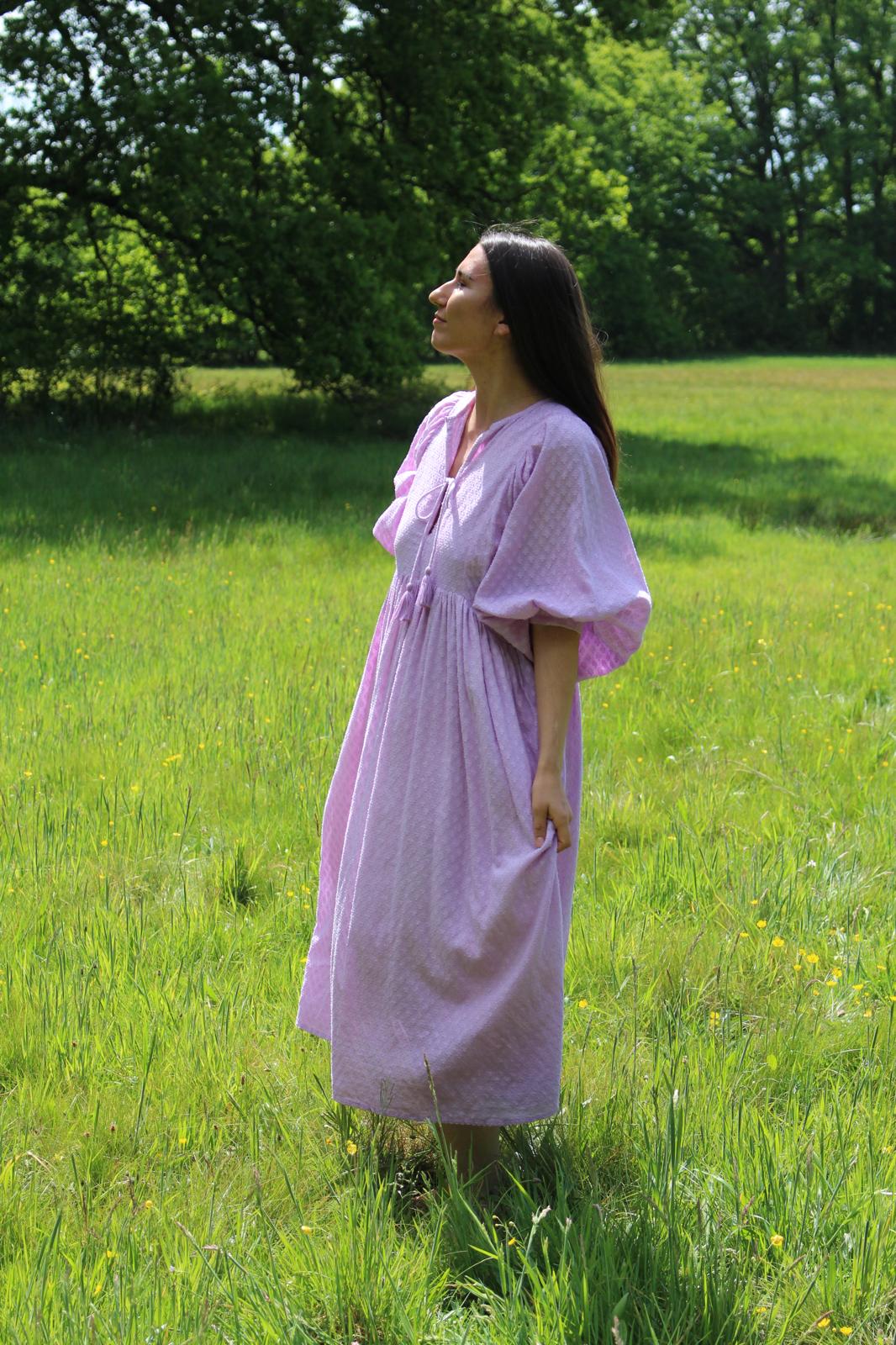 Lucia Kleid in zartem Fliederton, ideal für alltägliche Anlässe, umgeben von einer blühenden Wiese.