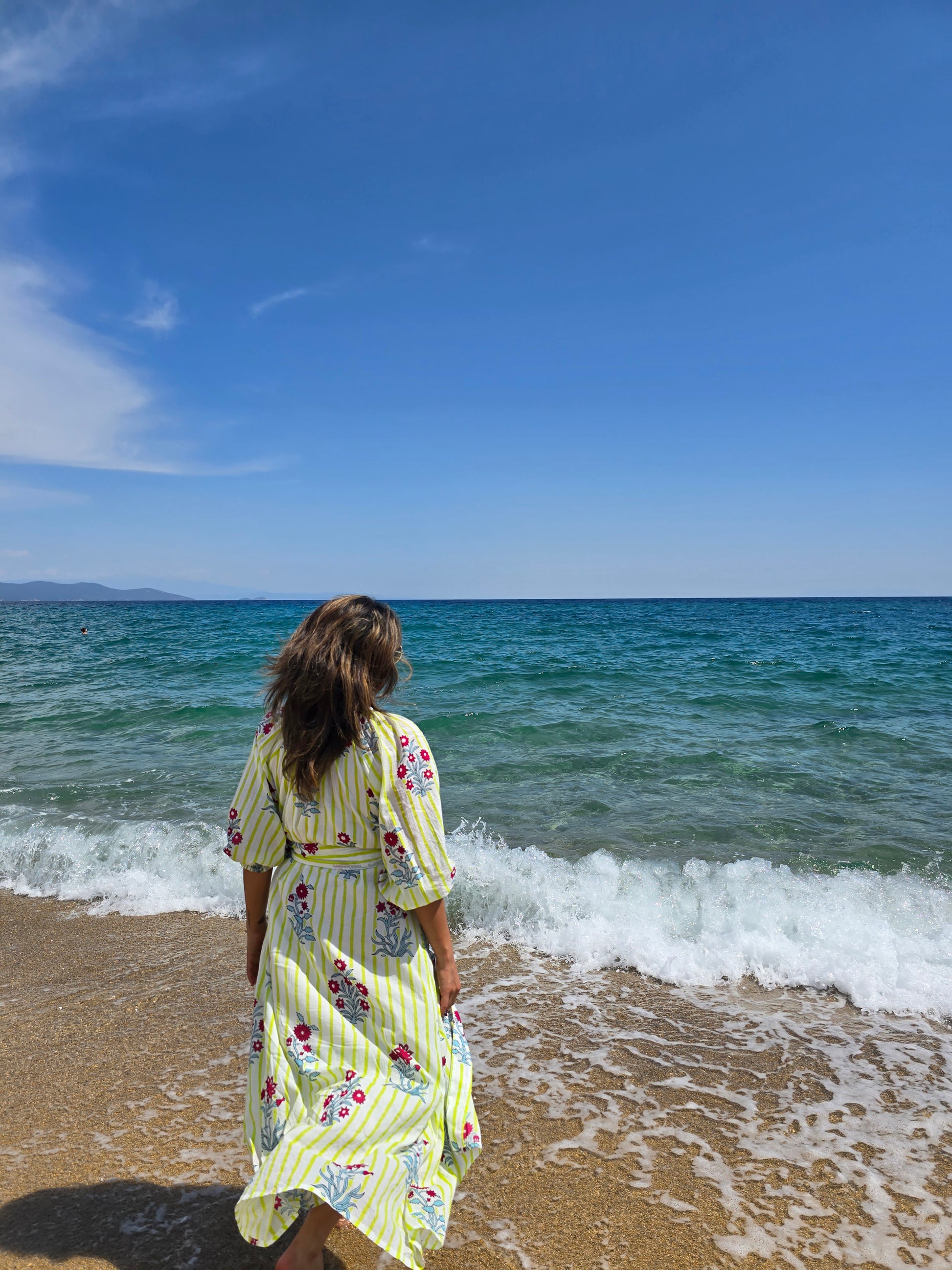 Rumi – Handbedrucktes Baumwollkleid am Strand, fröhliches florales Muster in lebhaften Farben.