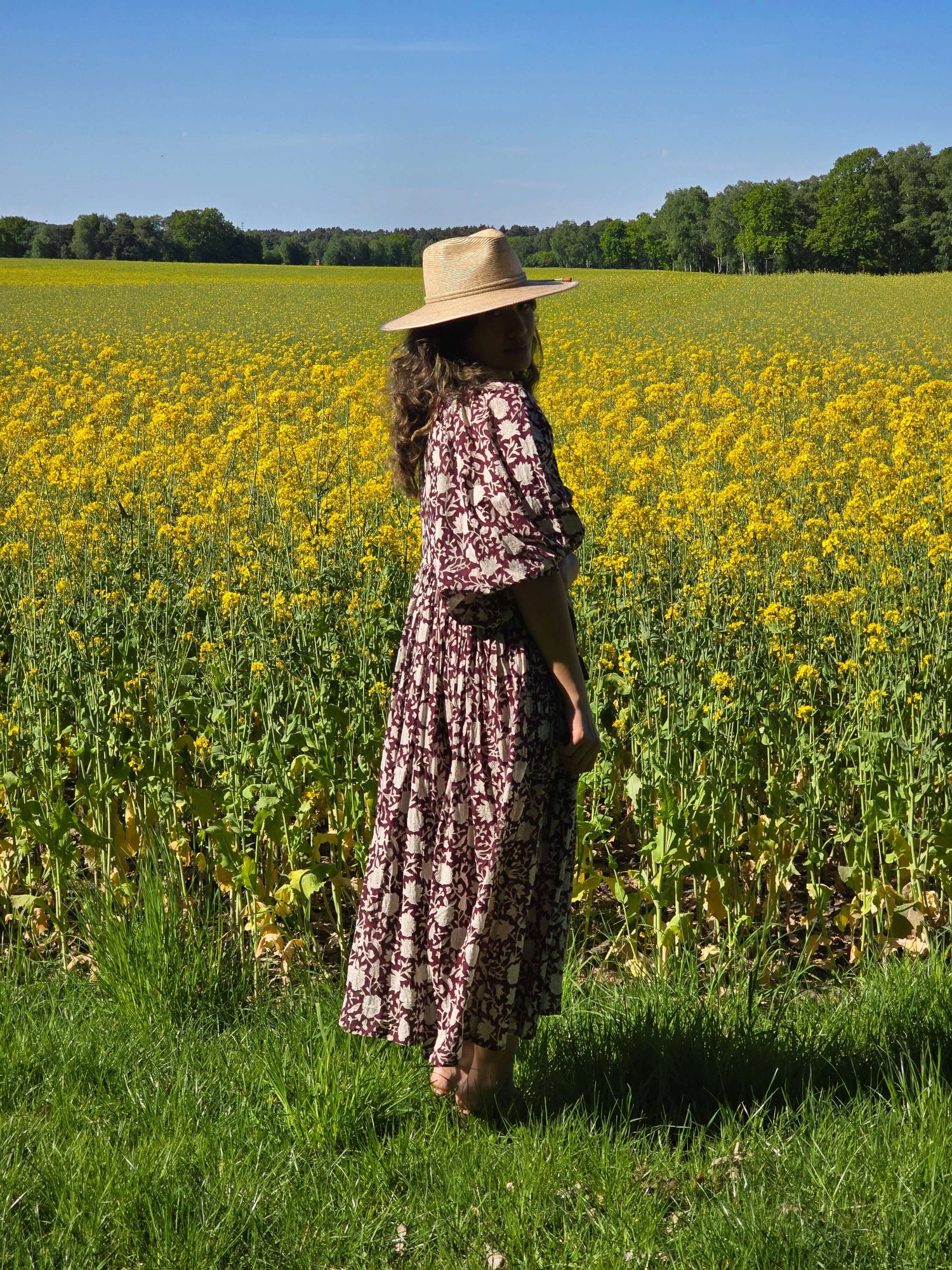 Camilla Kleid mit Handblockdruck – Burgundy in einer blühenden Wiesenlandschaft mit einer Person im Vintage-Stil.