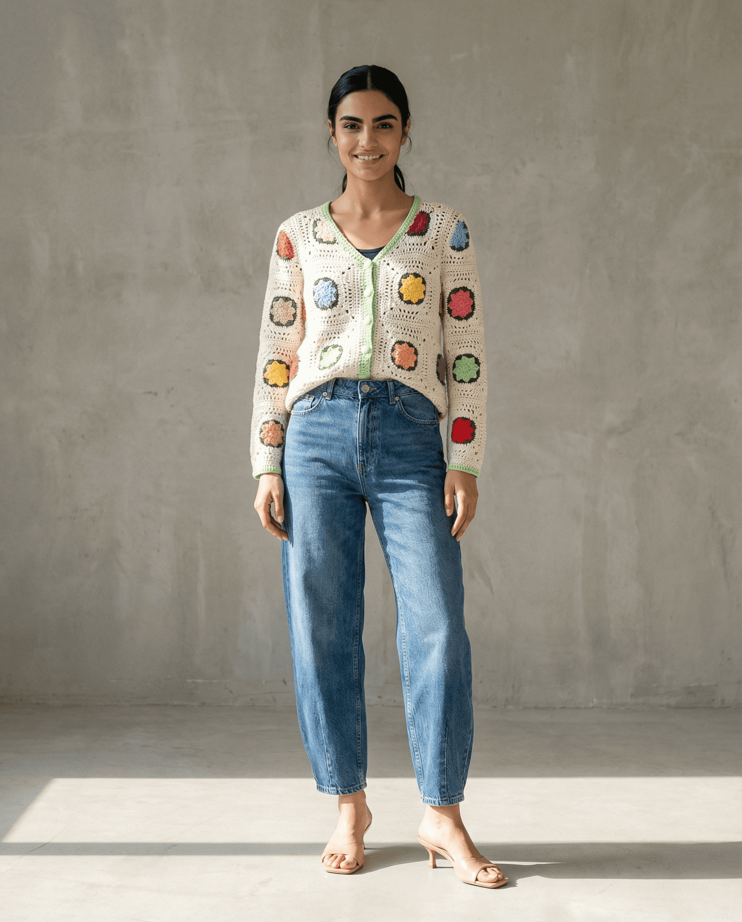 Handgemachte Strickjacke in buntem Patchwork-Design, kombiniert mit lässigen Jeans und Sandalen.
