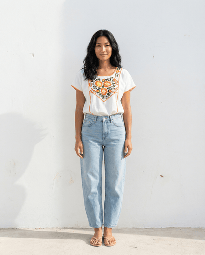 Handbestickte Carmela Bluse Nr. 15 – Creme/Orange getragen von einer Frau vor weißem Hintergrund.