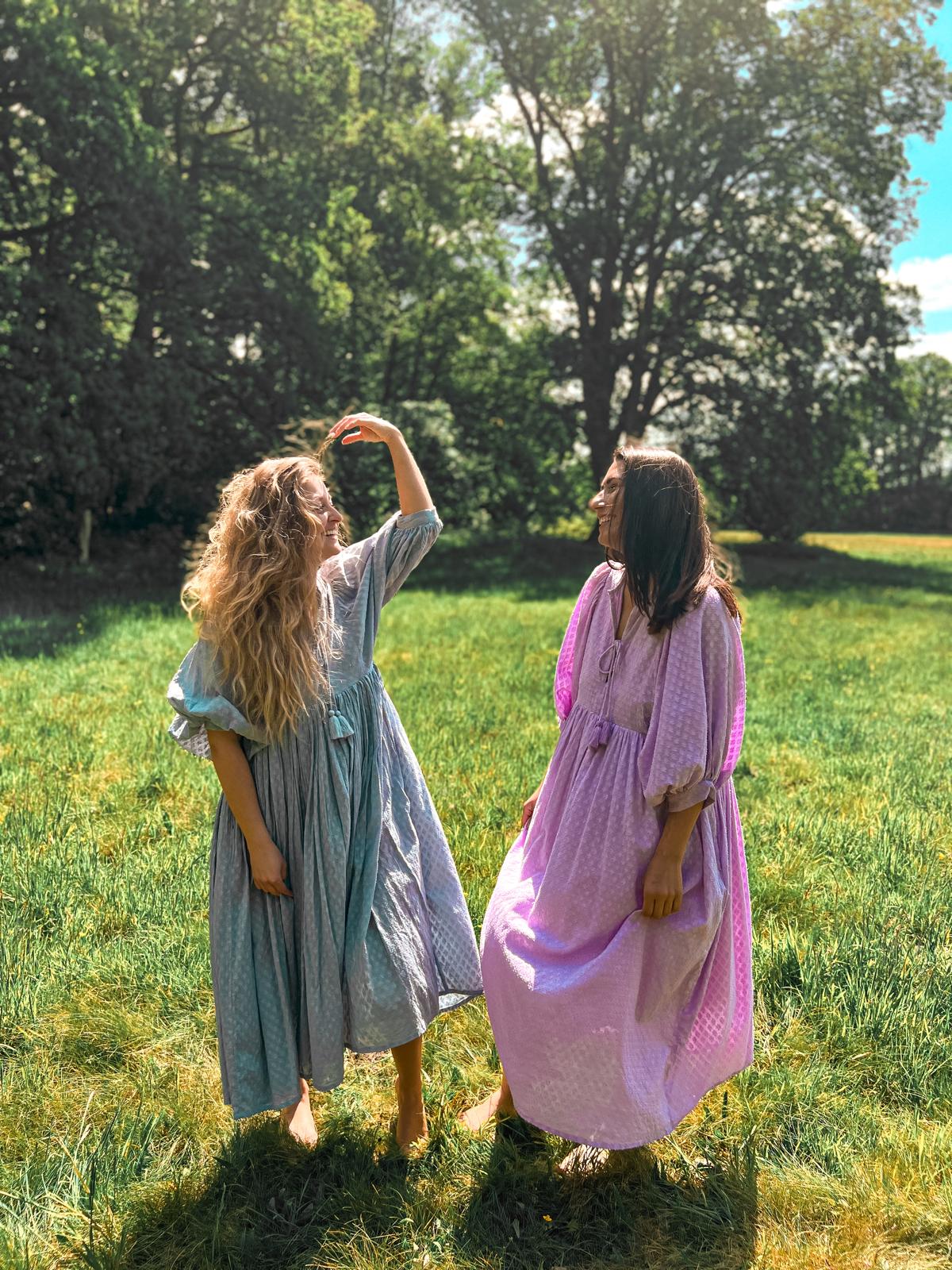 Zwei Frauen im Freien, die Lucia Kleid - Lila und ein weiteres Modell tragen, handgefertigt, Slow Fashion im Trend.