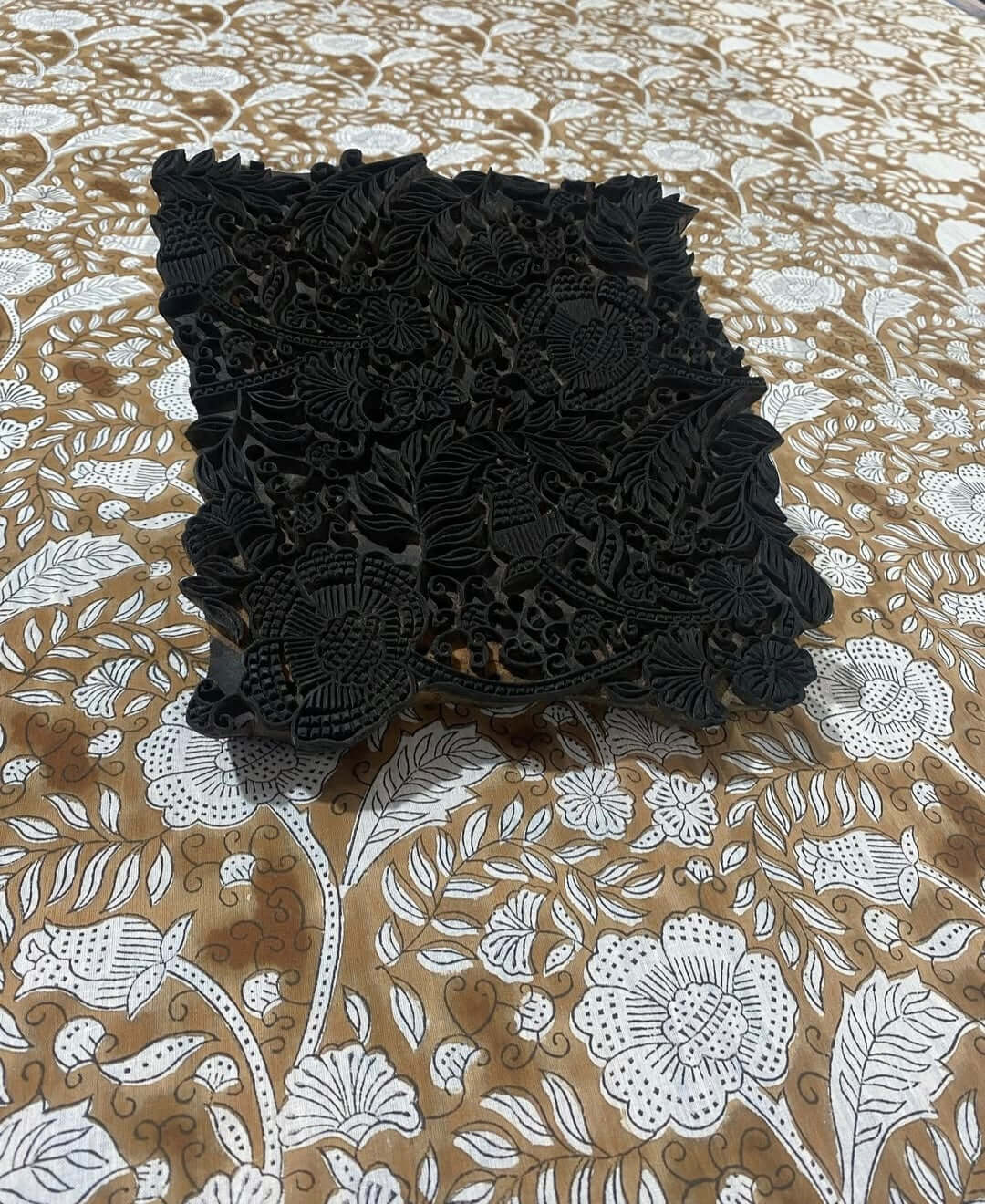 Detailaufnahme eines handgefertigten Blockdrucks auf einem braunen Stoff mit floralen Mustern.