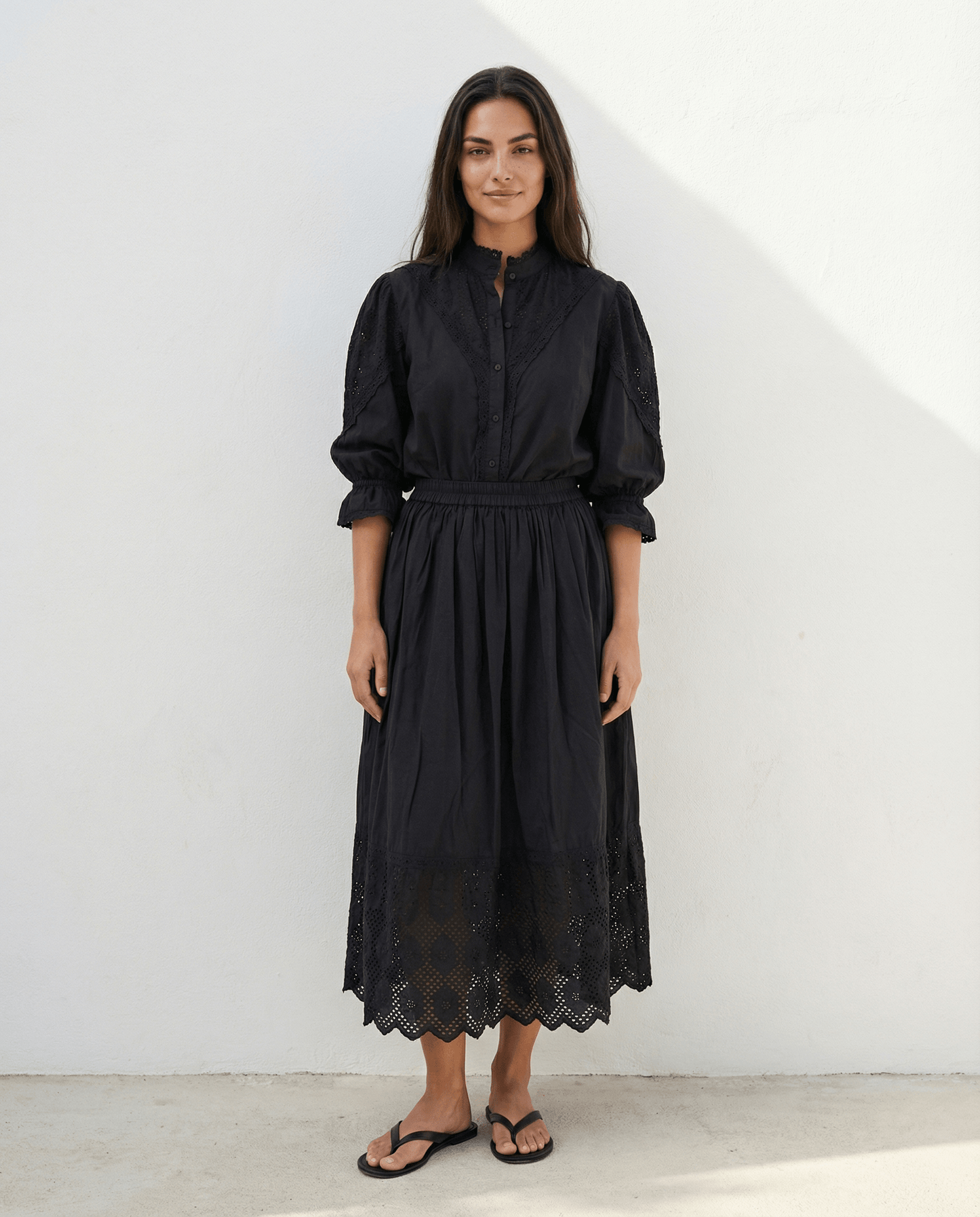 Woman wearing a long black cotton skirt with elastic waistband, lace trim hem and side pockets, lightweight flowing summer skirt