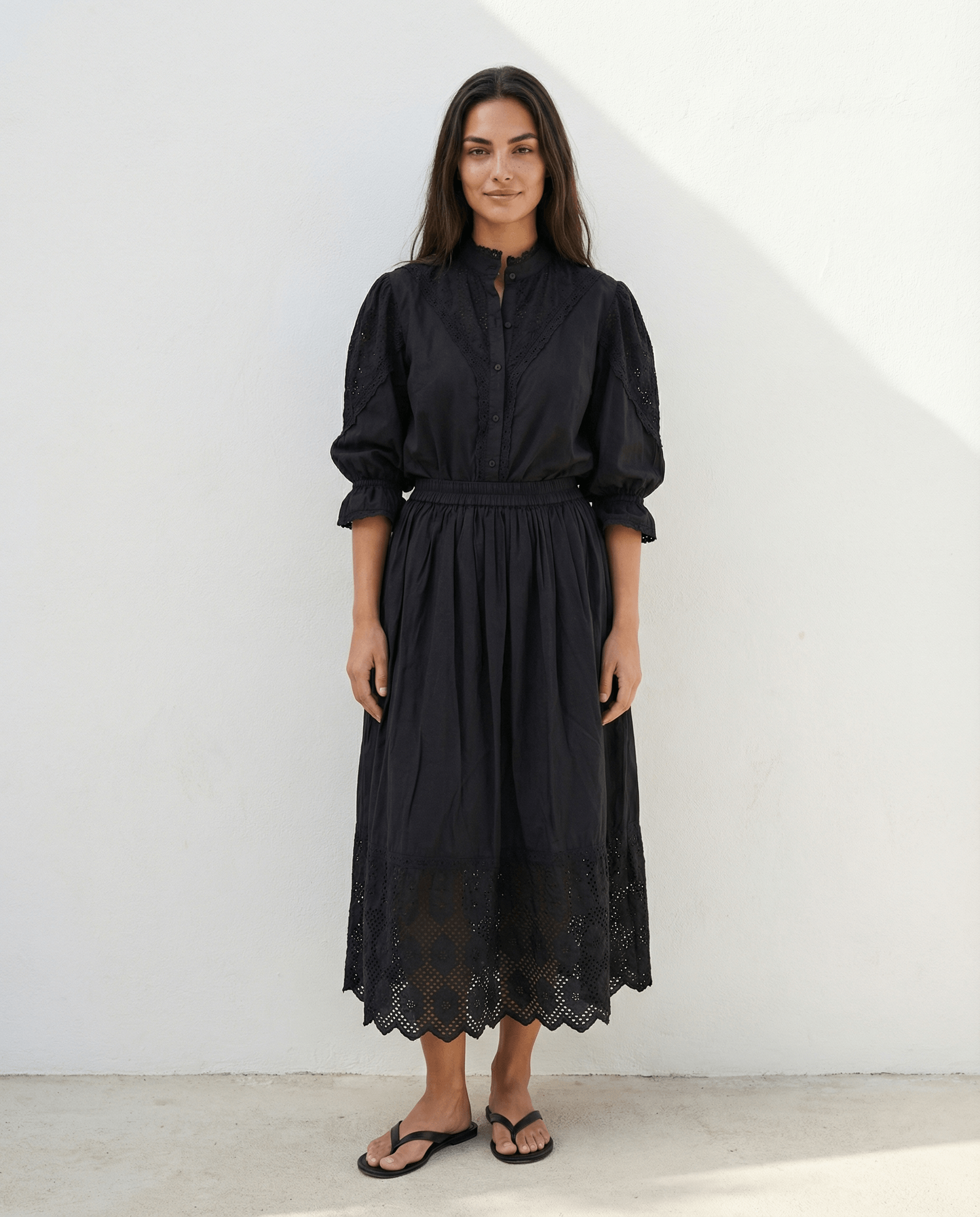 Woman wearing a long black cotton skirt with elastic waistband, lace trim hem and side pockets, lightweight flowing summer skirt