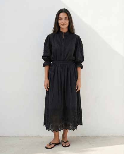 Woman wearing a long black cotton skirt with elastic waistband, lace trim hem and side pockets, lightweight flowing summer skirt